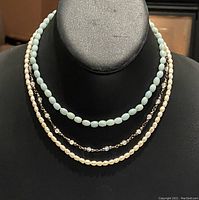 Three chokers displayed on black bust, showing the pearl, blue bead, and mixed bead designs.