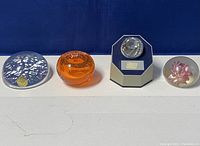 Front view showing all three paperweights lined up: clear snowflake, orange with bubbles, lucite floral.