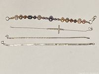 Four silver bracelets displayed straight, showing pearl bracelet, cross chain, and two snake chains