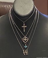Four sterling silver necklaces displayed on a black bust showing distinct pendants: cross, MOM heart, blue flower, LOVE letters.