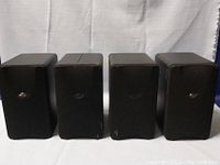 Front view of four Mini Mirage speakers with fabric grills showing minor wear.