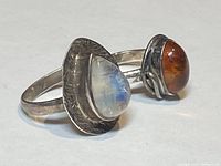 Two silver rings showing a pear-shaped opal ring and an amber ring side by side on a white background.