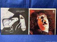 Photo of two vinyl record covers placed side by side on a blue fabric background showing Andre Gagnon's album 'Left Turn' with white sneakers on cover and Joe Cocker's album 'With a Little Help From My Friends' with expressive portrait on cover.