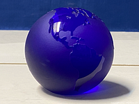 Cobalt blue glass globe paperweight photographed from side showing North and South America etched continents.