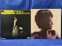 Two vinyl records with sleeves displayed side by side. Dionne Warwick 'Valley of the Dolls' album on the left, Nancy Wilson 'Tender Loving Care' album on the right.