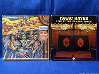 Two double-album vinyl records side by side: 'Ain't Misbehavin'' and 'Live at the Sahara Tahoe' by Isaac Hayes.