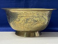 Side view of large brass footed bowl showing wide rim and etched dragon design.