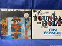 Photo showing front covers of MFSB Love Is The Message and Young-Hole Unlimited On Stage vinyl records, set side by side on a blue background.