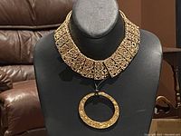 Wide collar-style gold-tone necklace displayed on bust form