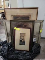 Lot of four framed art pieces stacked together with visible wear and protective plastic underneath.