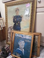 Photo showing a large framed military portrait with gold gilt frame and two smaller framed items including a bamboo framed vintage advertisement and a three-dimensional artwork.