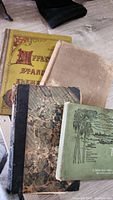 Top view of four antique books stacked, showing covers and edges, some wear visible