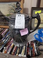 Front and side view of the antique glass-lined coffee pot with floral embossed handle and decorative lid finial, showing tarnished silver-tone finish.