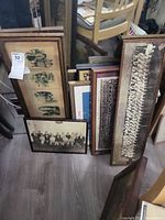 Multiple frames of antique photographs and wall art stacked together on floor showing a variety of framed antique images