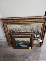 Three paintings grouped, ornate gilt frame at back and two smaller framed alpine scenes in front
