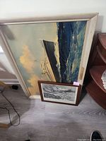 Wide view of the 23x34 inch SS Nieuw Amsterdam ocean liner canvas in white frame leaning against the wall with the smaller framed wreck of The Atlantic print in front.