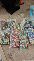Eight bags of marbles on floor showing various colors and patterns including solid and swirled marbles