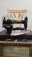 Photo showing side view of the black White Rotary sewing machine on wooden base with an instruction pamphlet and spool of thread placed in front.