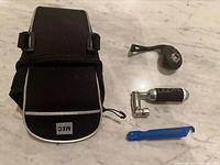 Top-down view of four bike accessories: MEC under-seat bag, Lezyne CO2 inflator and cartridge, MEC rechargeable light, and blue Park Tool tire lever arranged on a surface.