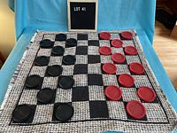 Photo showing full woven cloth checkers board with black and white checkered pattern and oversized black and red checkers pieces arranged on board.