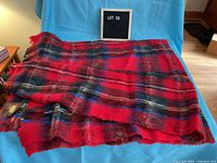 Photo of vintage Eaton's throw blanket showing red, black, blue, and green plaid pattern, spread on blue background with original tag visible