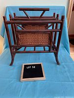 Front and side view of wood and cane magazine rack showing dark wooden frame and woven cane panels on a blue backdrop.