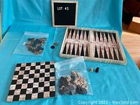 Photo of marble chessboard, chess pieces in plastic bag, small bag of coins, and marble backgammon board on a turquoise cloth.