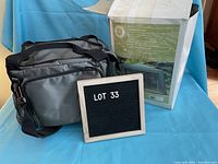 Gray cooler bag with multiple compartments and adjustable shoulder strap placed on blue fabric background, with original mosquito net packaging visible in the background.