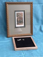 Framed numbered print, gold frame with decorative edge, image of autumn house scene visible inside matting.