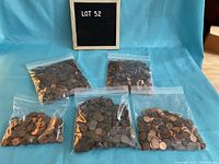 Five resealable plastic bags filled with US pennies on a blue cloth background, labeled Lot 52.