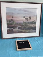 Front view of the framed print showing the landscape artwork and palm trees under a sunset sky with the artist's signature.
