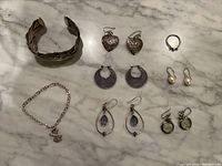 All jewelry items together on marble surface showing the full lot – cuff bracelet, charm bracelet, multiple pairs of earrings, ring.