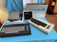 Full lot view including Commodore 1541 floppy disk drive in styrofoam, beige VIC-20 keyboard, dark grey Commodore keyboard, and original cardboard box labeled SINGLE FLOPPY DISK.
