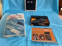 Photo showing two vintage home hair trimming sets: Raycine Home Hair Trimming Set in worn packaging on left and Philips Mr. Trim cordless hair trimmer in original box with instruction booklet on right, on blue background.