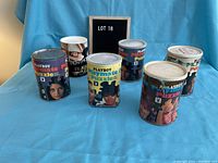 Photo showing seven Playboy Playmate puzzle cans and one Penthouse puzzle can on a blue cloth backdrop with lot label