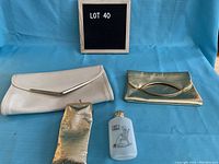 Front view showing two vintage purses—a white clutch and a metallic gold clutch—with a small gold-colored carrying case and frosted glass flask with golfer engraving, against a blue background.