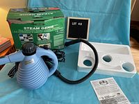 Vintage Steam Genie handheld steam cleaner with original green box, foam insert, and instruction manual, displayed on blue backdrop.