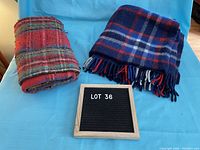 Two folded vintage throw blankets placed side by side on a light blue surface, one red plaid and one blue plaid.