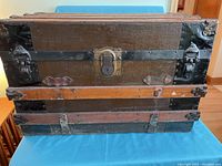 Front view of vintage travel trunk showing central lock, metal hardware, wooden slats, and wear.