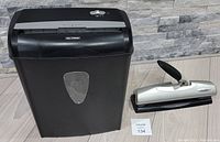 Full view of the black 8-sheet cross-cut shredder next to the silver and black Swingline hole punch on the floor.