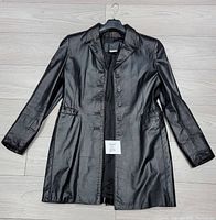 Front view of the black leather coat laid flat showing the lapel collar, button closure, and side pockets.