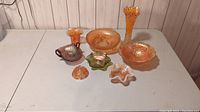 Lot of eight carnival glass pieces including bowls, vases, and dishes in various colors such as amber, peach, green, and pink with iridescent finishes.