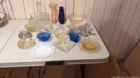 Full lot overview on table showing multiple glass pieces including plates, bowls, serving trays, and vases of various colors and styles