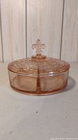 Front view of pink glass 3-part candy dish with fleur-de-lis handle on lid, showing condition and design