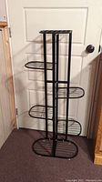 Front view of black metal plant stand showing curved shelves on either side.