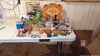 Wide view of the table with mixed vintage items including toys, decorative objects, glassware, and boxes.