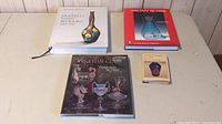 Four glass-related books displayed on a table, including three hardcover collector books and one small paperback book.