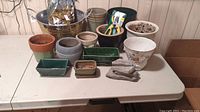 Table displaying multiple planters of various materials and sizes along with the hand pruners and a bag of macroplugs plant starters.