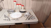 Wide table view showing glass canisters, Anchor Hocking milk glass tray, a glass bakeware casserole dish with lid, aluminum serving dish with removable glass inset, Jello mold, and metal kitchen tools.