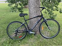 Full side view of the black Genesis Trafik 0.5 SE 7-speed urban/hybrid bike leaning against a tree outdoors